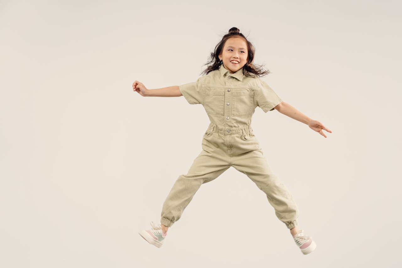 Happy young girl in a jumpsuit jumping joyfully against a plain white background.