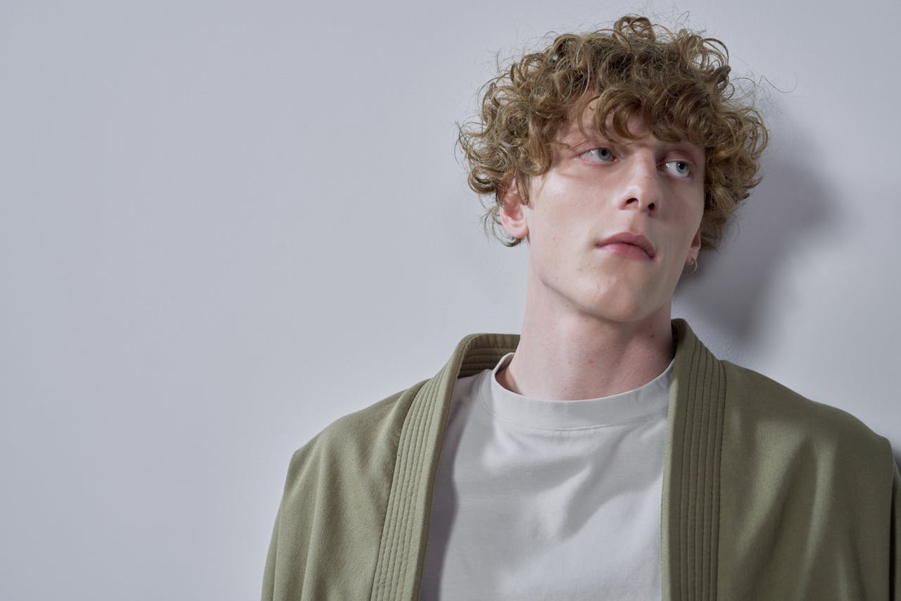 Modern portrait of a curly-haired man in casual clothing against a gray background.