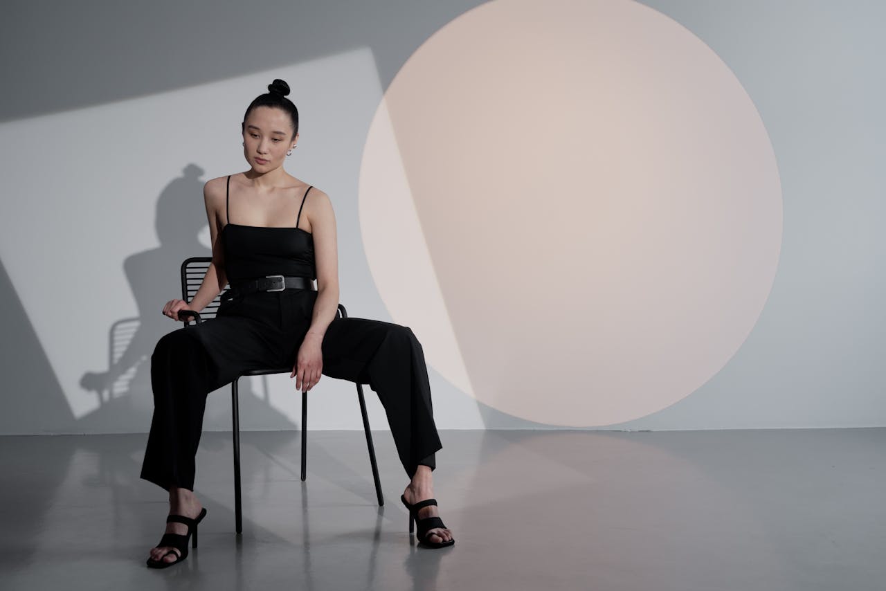 Portrait of an Asian woman in a stylish jumpsuit seated against a geometric backdrop.